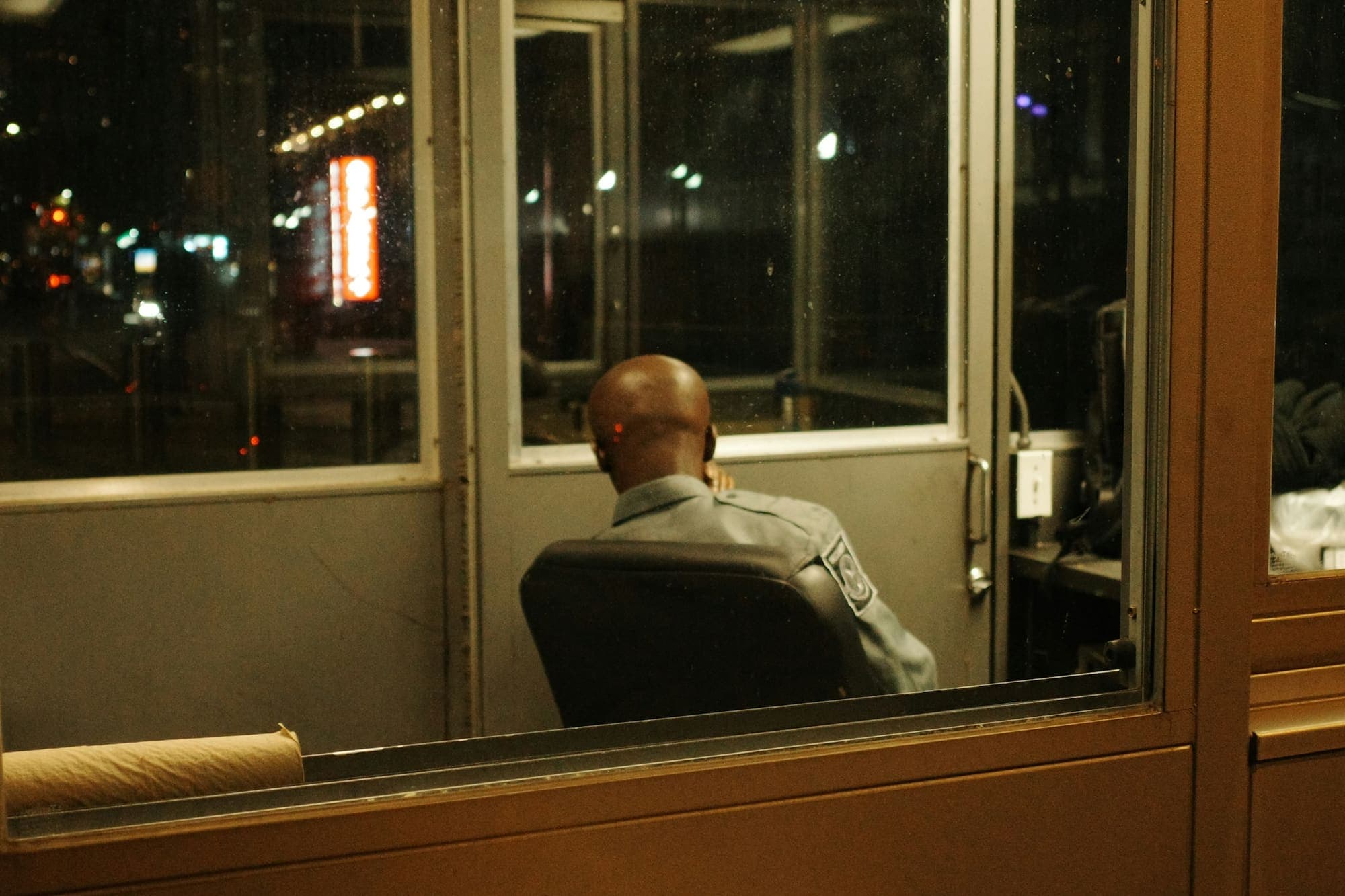 Un guardia de espaldas en su caseta, de noche, frente a los vidrios